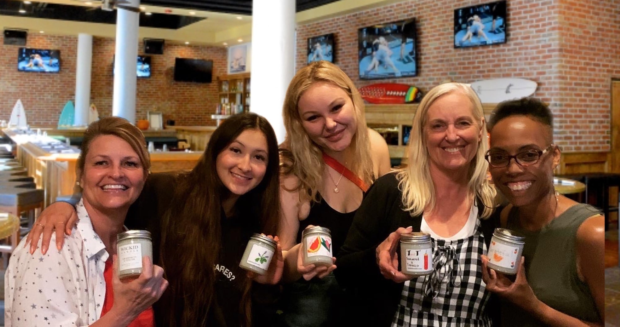 Five adults displaying completed Wickid candles in a wine-shop Workshop setting